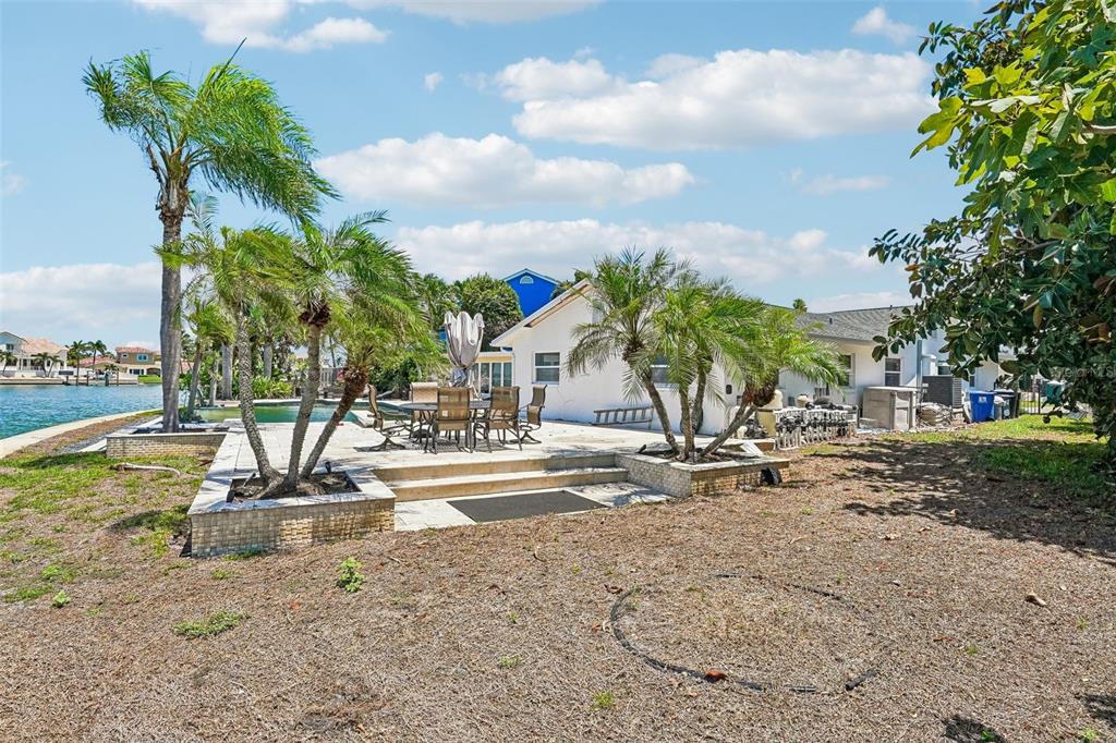 A backyard patio with a dining set, palm trees, and a view of the water — 8078 13TH AVENUE S, ST PETERSBURG, FL