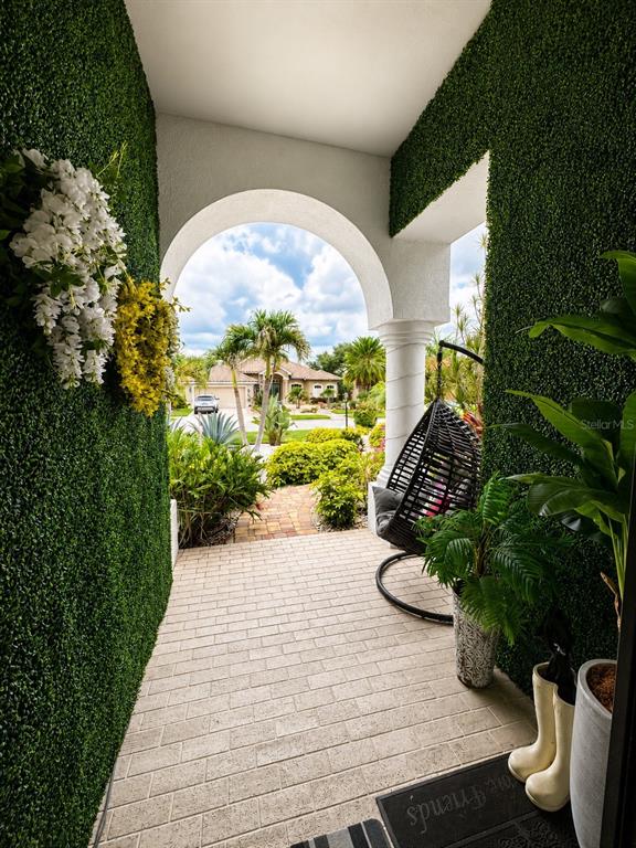A covered entryway features artificial grass walls, a hanging chair, and a brick-paved floor — 810 OAK BRIAR LANE, OSPREY, FL