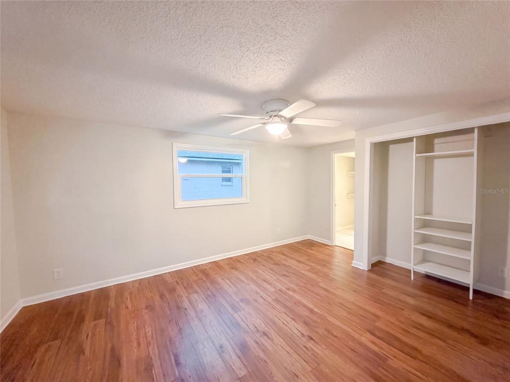 A bedroom with wood-look flooring, a ceiling fan, a window, and built-in closet shelving — 3004 HUNKIN CIRCLE, DELTONA, FL