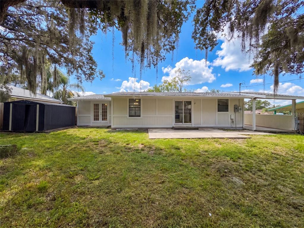 The rear exterior of a single-story house features a concrete patio and a storage shed — 3004 HUNKIN CIRCLE, DELTONA, FL
