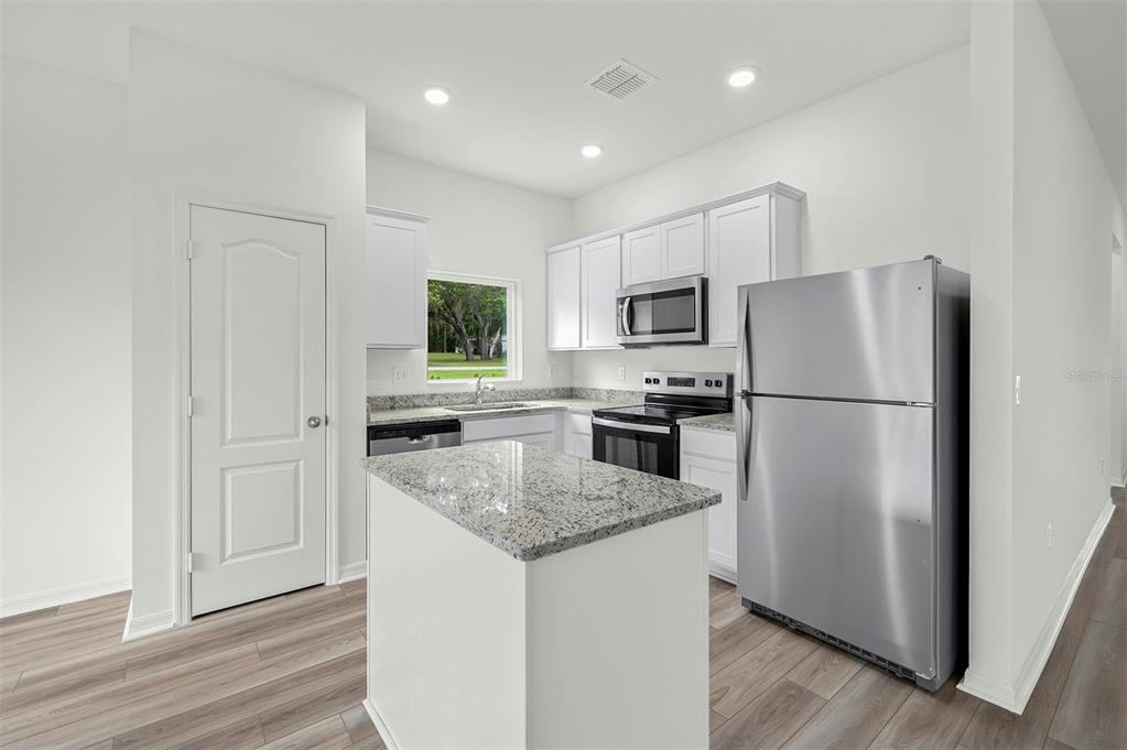 A kitchen features white cabinets, granite countertops, stainless steel appliances, and a central island — 13276 TULA LOOP, ASTATULA, FL