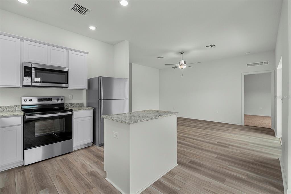 A kitchen with white cabinets, stainless steel appliances, and a granite-topped island overlooks an open room — 13276 TULA LOOP, ASTATULA, FL