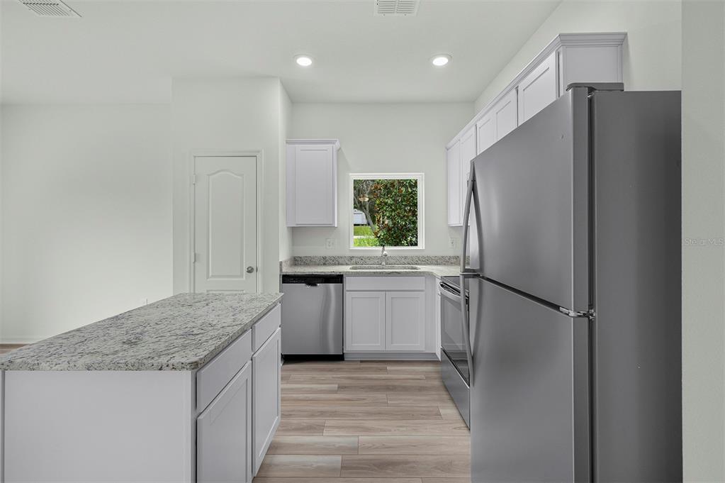 A kitchen features white cabinets, granite countertops, stainless steel appliances, and a central island — 13276 TULA LOOP, ASTATULA, FL