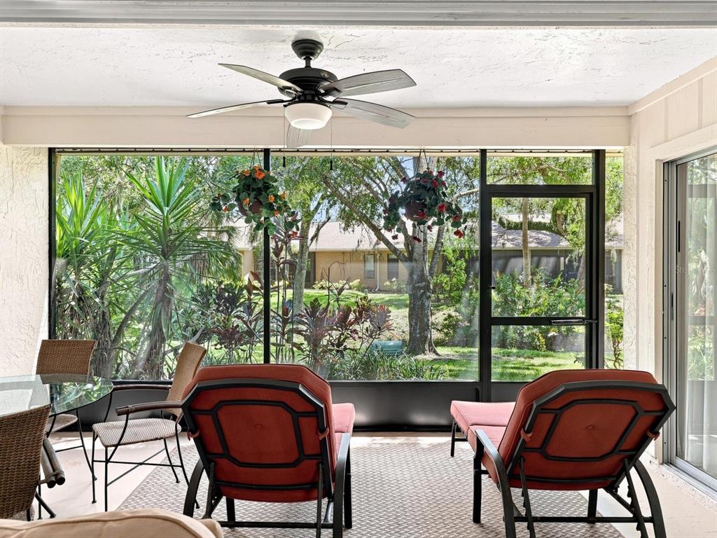 A screened-in patio features a ceiling fan, outdoor furniture, and views of trees and landscaping — 3450 TALLYWOOD LANE UNIT 7150, SARASOTA, FL