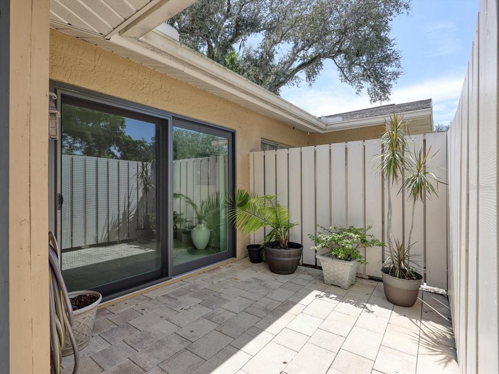 A paved patio features a sliding glass door, potted plants, and a white privacy fence — 3450 TALLYWOOD LANE UNIT 7150, SARASOTA, FL