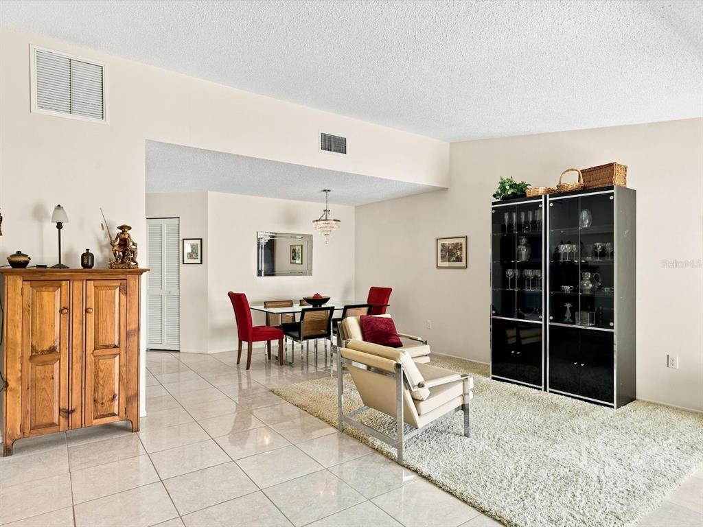 A living and dining area features tile flooring, a beige area rug, and a glass cabinet — 3450 TALLYWOOD LANE UNIT 7150, SARASOTA, FL