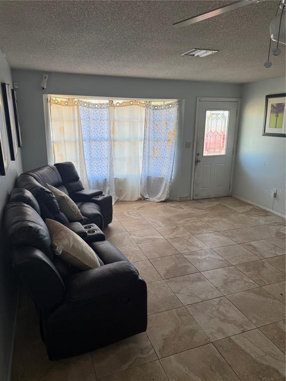 A living room features light-colored tile flooring, a dark leather sectional sofa, and a front door — 750 NE HAMPTON DRIVE, PALM BAY, FL