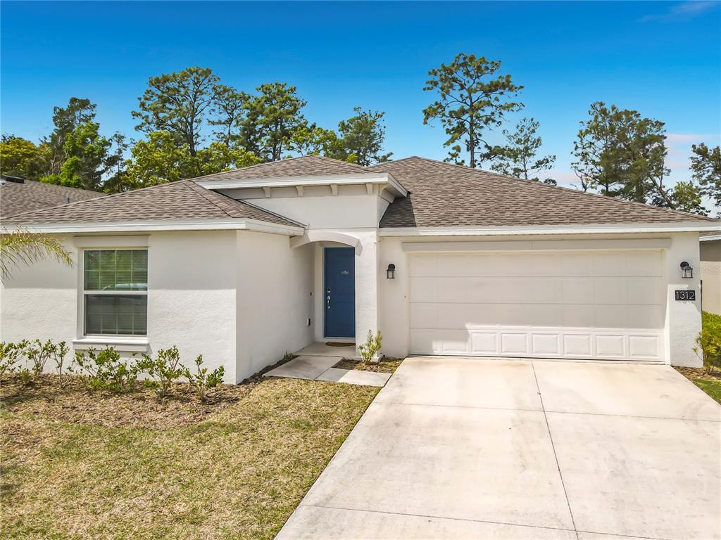 A single-story house with a white stucco exterior, blue front door, and two-car garage — 1312 PEACH CREEK DRIVE, OSTEEN, FL