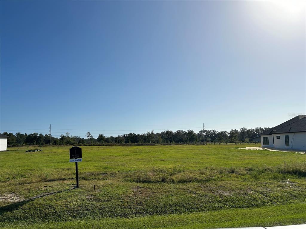 A vacant grassy lot with a real estate sign stands next to a residential house — 5111 SW 125TH CIRCLE, ARCHER, FL