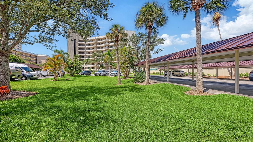 A grassy lawn sits in front of a multi-story building and a covered parking structure — 5880 MIDNIGHT PASS ROAD UNIT 307, SARASOTA, FL