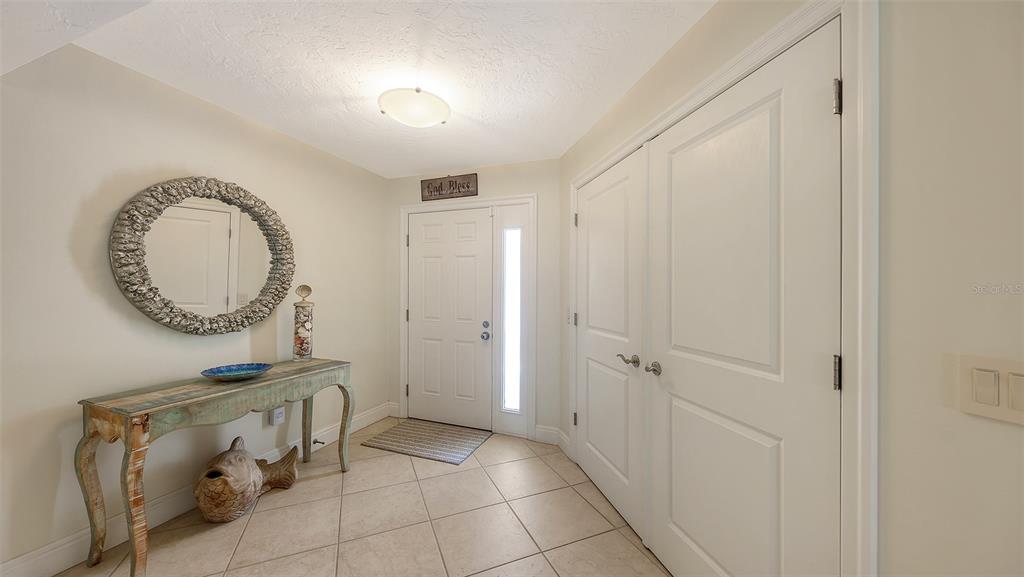 An entryway features a console table, a round mirror, and double doors on tiled flooring — 5880 MIDNIGHT PASS ROAD UNIT 307, SARASOTA, FL