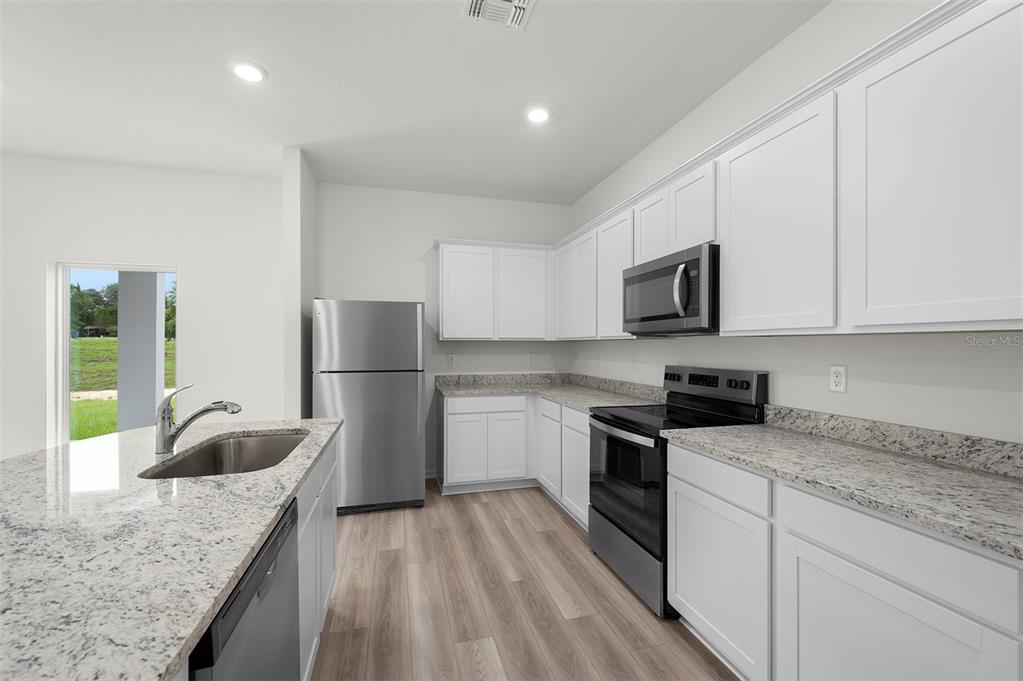 A kitchen features white cabinets, granite countertops, stainless steel appliances, and light wood-look flooring — 13280 TULA LOOP, ASTATULA, FL