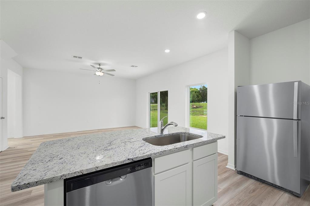 A kitchen island with a granite countertop and stainless steel sink faces an open living area — 13280 TULA LOOP, ASTATULA, FL