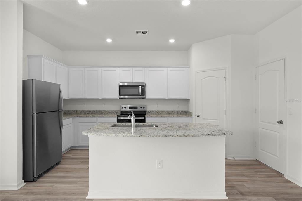 A modern kitchen features white cabinets, granite countertops, a center island, and stainless steel appliances — 13280 TULA LOOP, ASTATULA, FL