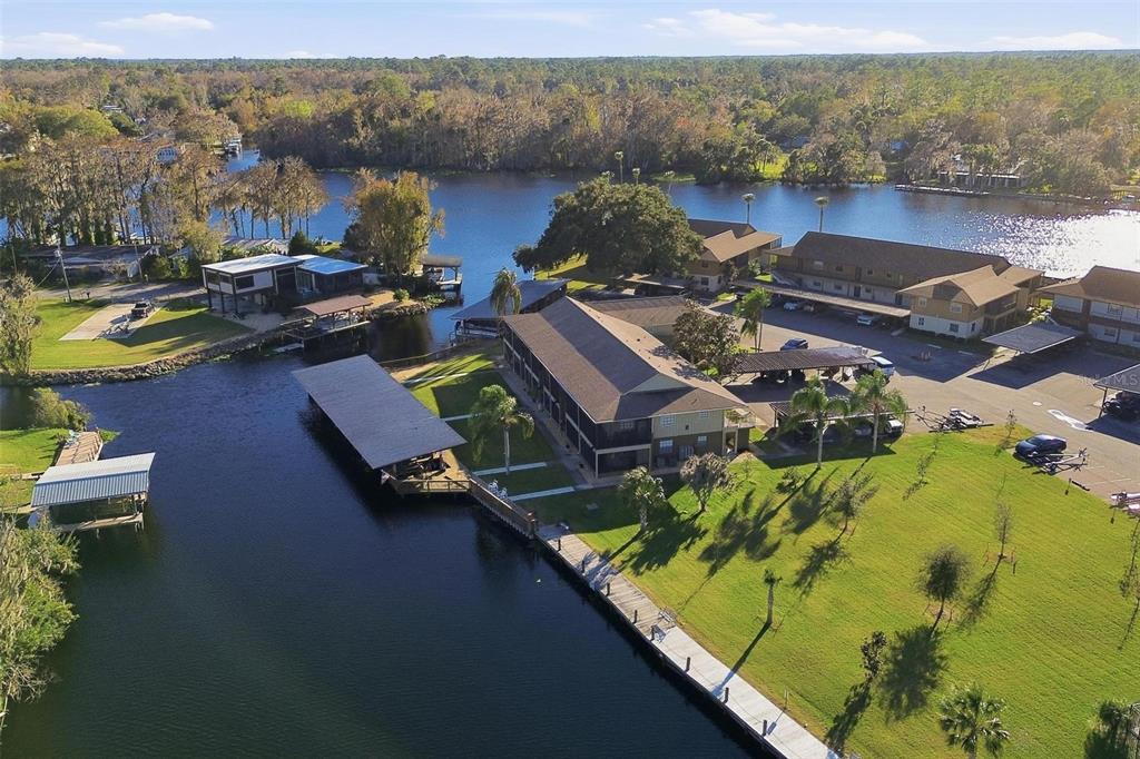 An aerial view shows a multi-story building with a boat dock along a river — 1640 JUNO TRAIL UNIT 101H, ASTOR, FL