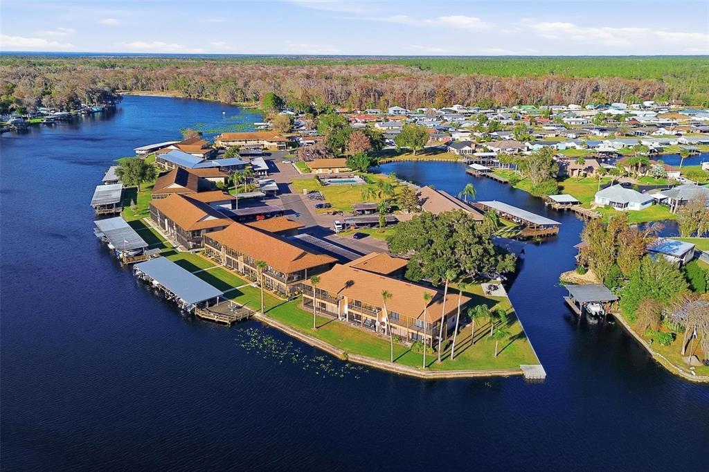 An aerial view shows a waterfront apartment complex with boat slips and a swimming pool — 1640 JUNO TRAIL UNIT 101H, ASTOR, FL