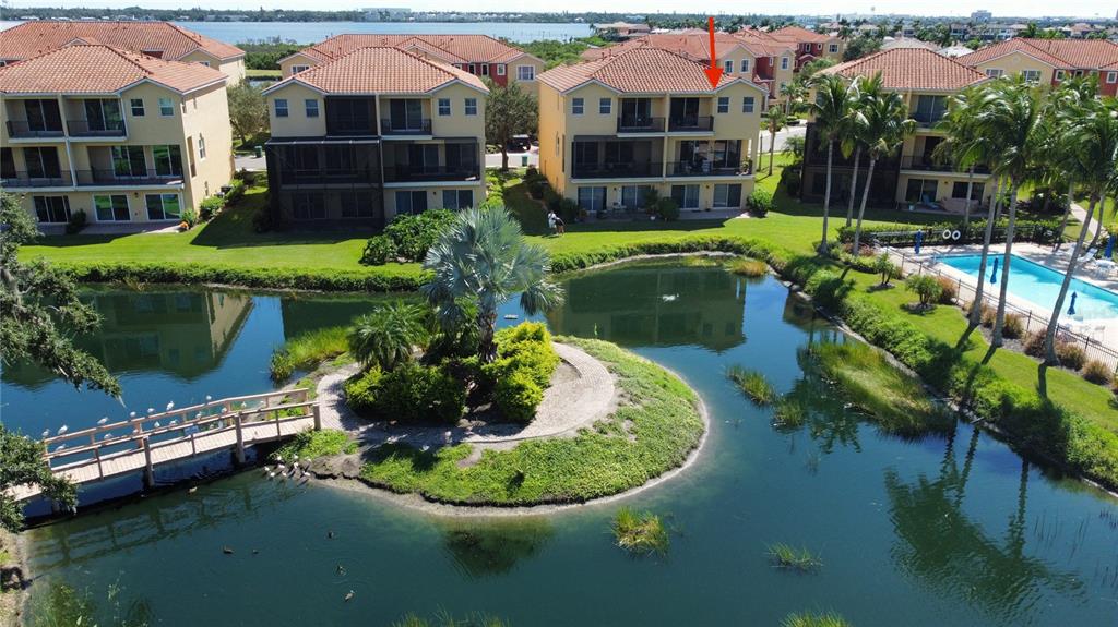 An aerial view shows a multi-story apartment building overlooking a pond with a small island — 1226 3RD STREET CIRCLE E, PALMETTO, FL