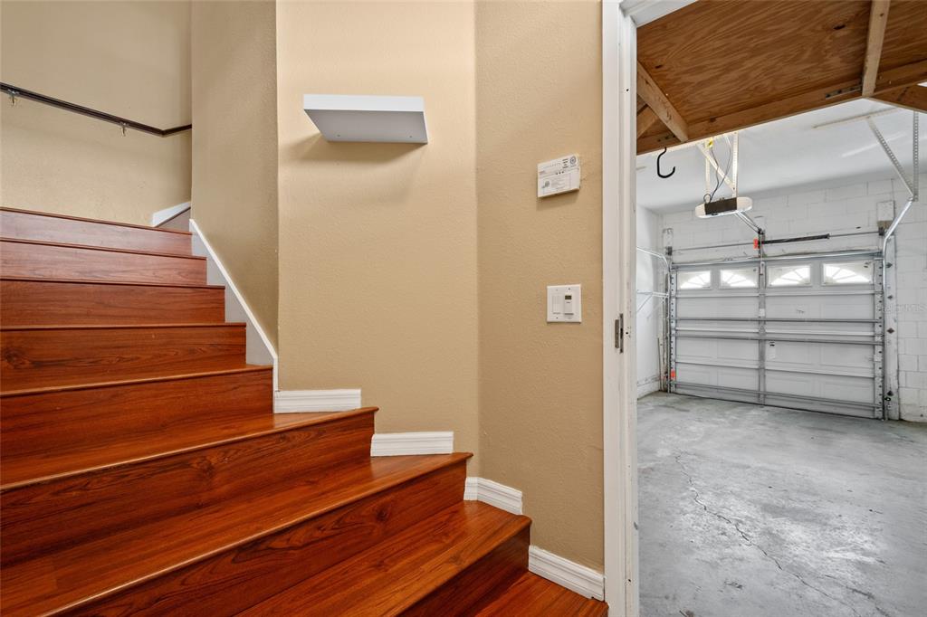 A wooden staircase leads upward next to an open doorway revealing a garage interior — 1937 ESTANCIA CIRCLE UNIT 1937, KISSIMMEE, FL