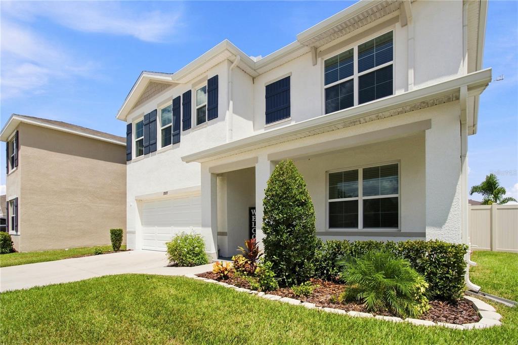 A two-story white house with a garage, front porch, and landscaped yard under a blue sky — 33635 HAMILTON HILL LANE, WESLEY CHAPEL, FL