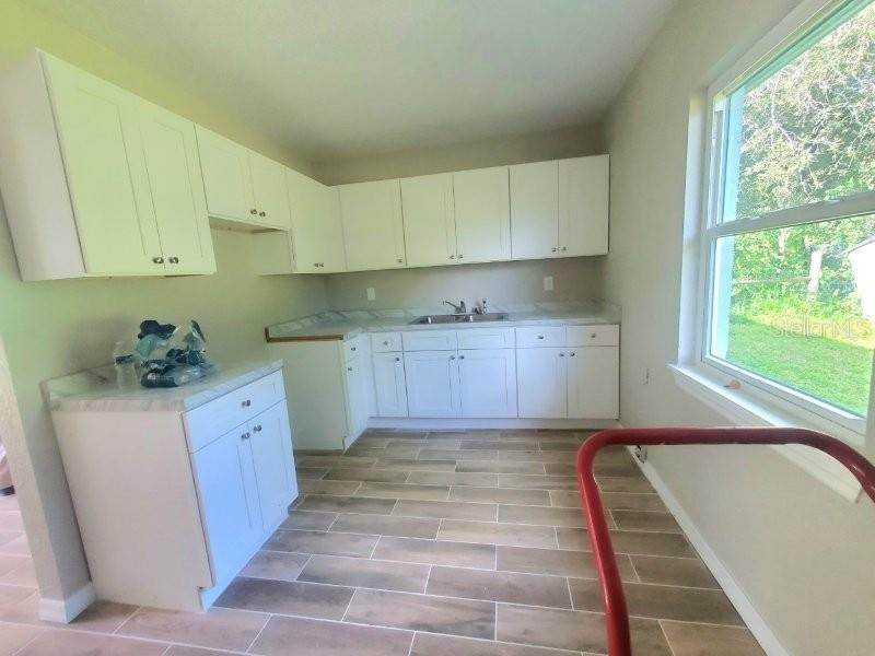 A kitchen features white cabinets, a stainless steel sink, and wood-look tile flooring — 420 SOMERSET ROAD, PUNTA GORDA, FL