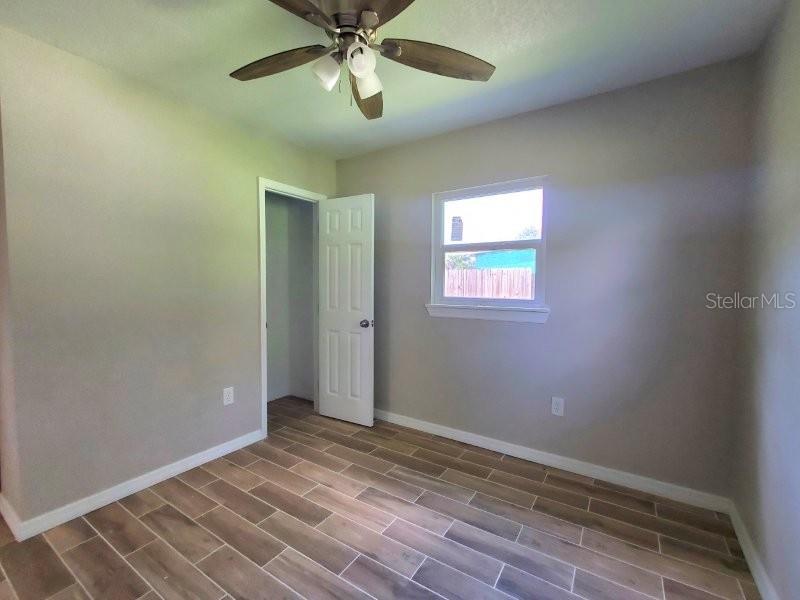 A bedroom with light-colored walls, wood-look tile flooring, a ceiling fan, and an open closet door — 420 SOMERSET ROAD, PUNTA GORDA, FL