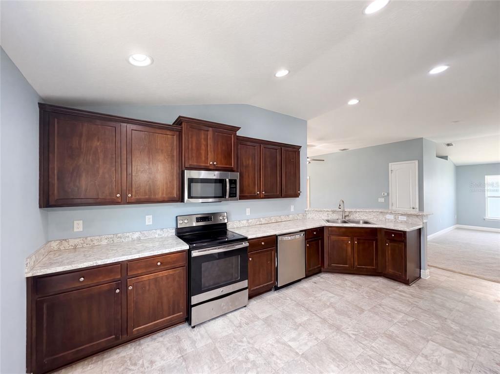 A kitchen features dark wood cabinets, stainless steel appliances, and light-colored countertops — 1229 LONGVILLE CIRCLE, TAVARES, FL