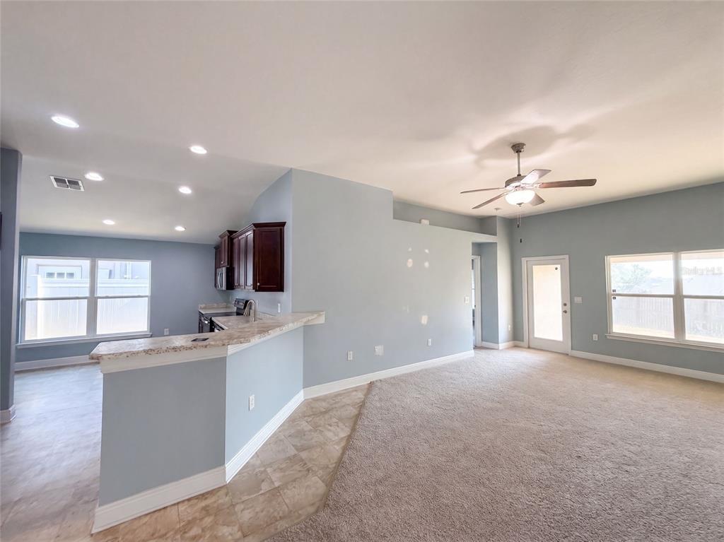 An open-concept living area features a kitchen with dark cabinets, granite countertops, and carpeted flooring — 1229 LONGVILLE CIRCLE, TAVARES, FL