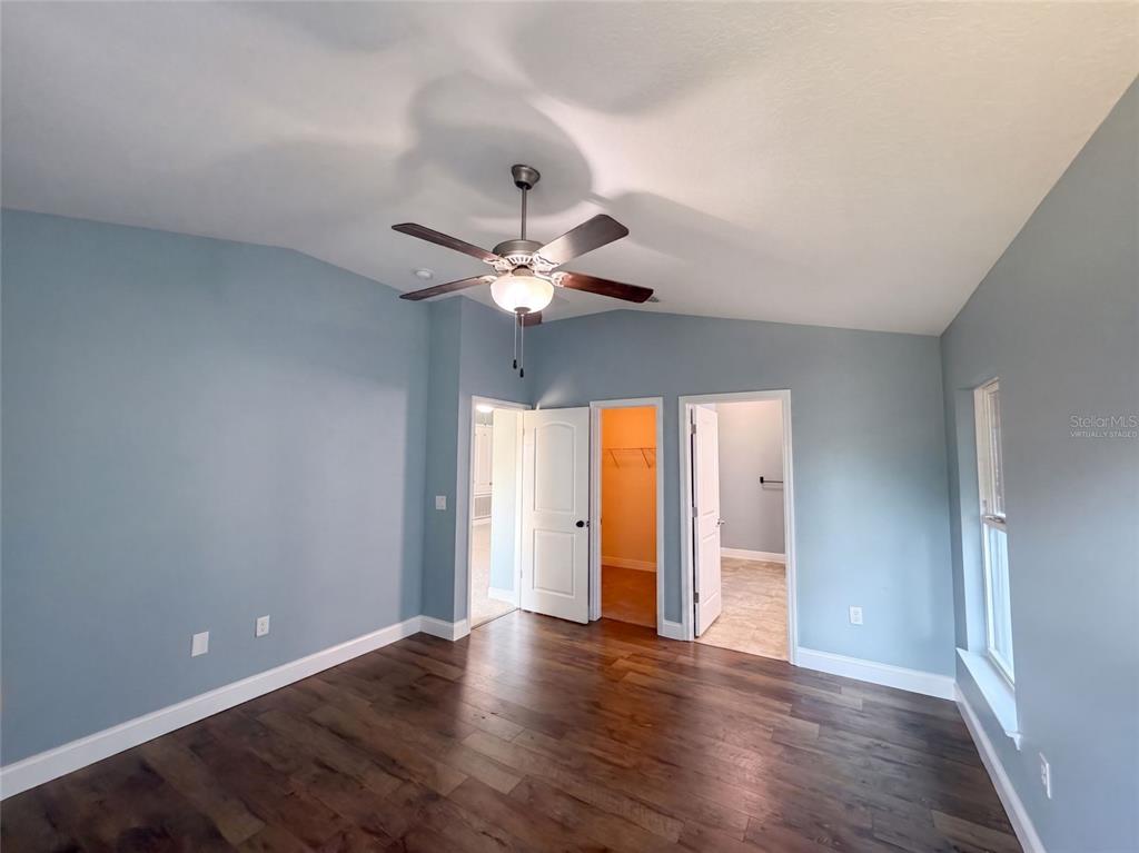 An empty bedroom features light blue walls, dark wood flooring, and a ceiling fan — 1229 LONGVILLE CIRCLE, TAVARES, FL
