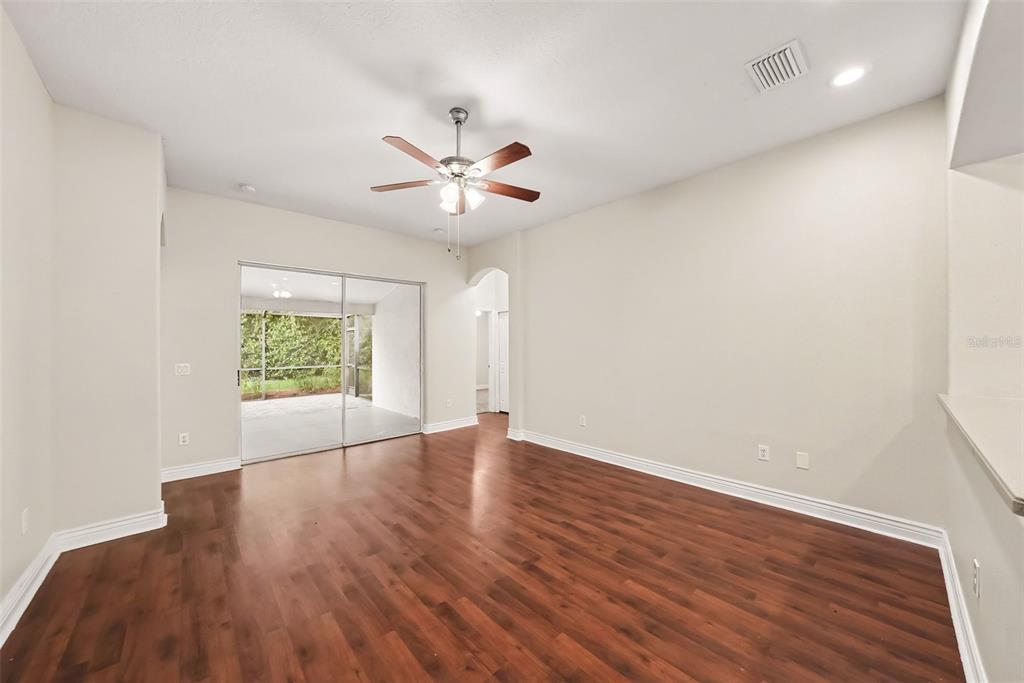 An empty living room features wood-look flooring, a ceiling fan, and sliding glass doors — 16312 BRIDGECROSSING DRIVE, LITHIA, FL