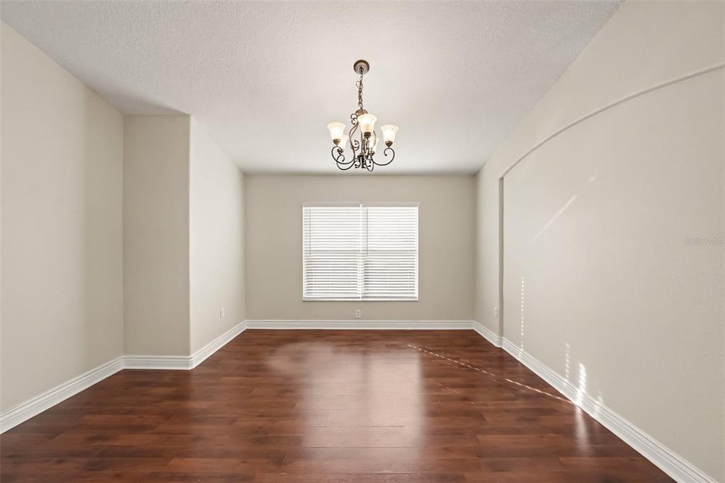 An empty dining room features dark wood flooring, a central chandelier, and a single window — 16312 BRIDGECROSSING DRIVE, LITHIA, FL
