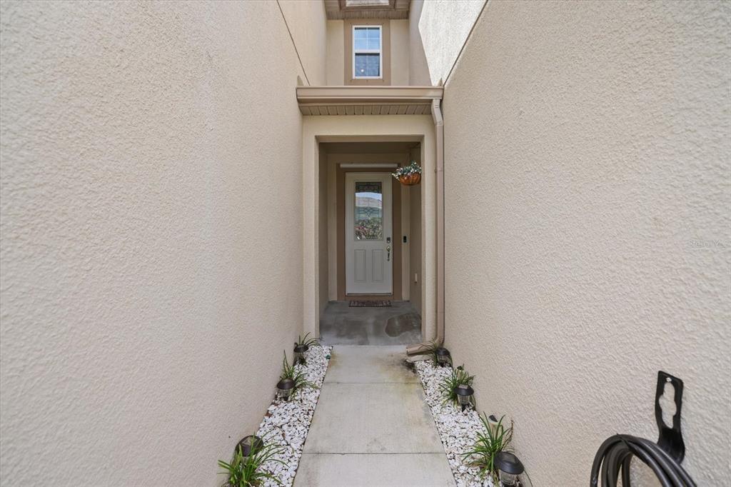 A narrow concrete walkway leads to a white front door between two stucco walls — 11814 SKY ACRES TERRACE, BRADENTON, FL