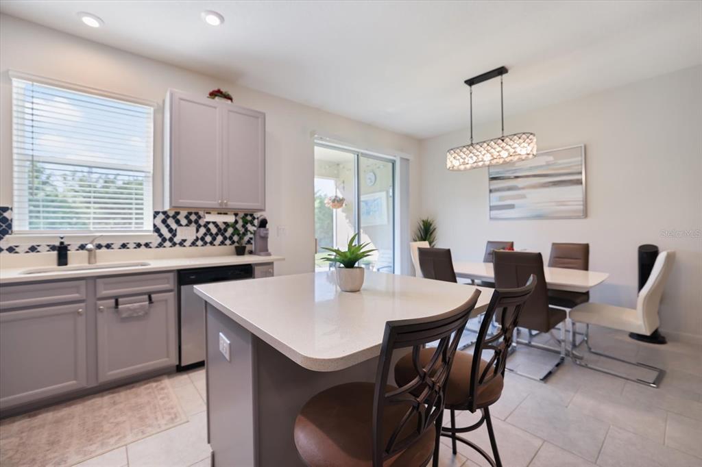 A kitchen features gray cabinets, a central island with bar stools, and an adjacent dining area — 11814 SKY ACRES TERRACE, BRADENTON, FL