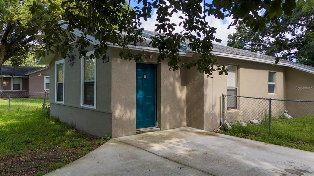A tan, single-story house features a teal front door and a concrete driveway — 713 22ND STREET, ORLANDO, FL