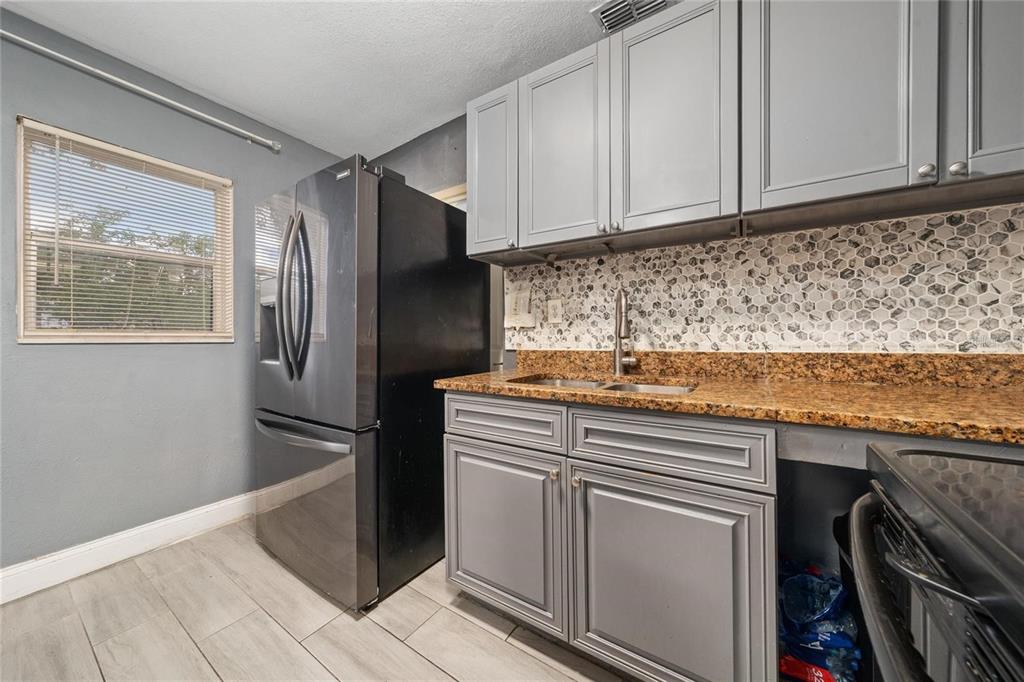 A kitchen features gray cabinets, a black refrigerator, granite countertops, and a hexagonal tile backsplash — 713 22ND STREET, ORLANDO, FL