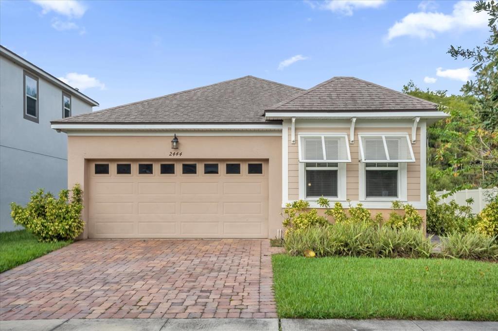 A side view of a house with tan siding, a dark door, and landscaped bushes — 2444 VARENNA LOOP, KISSIMMEE, FL