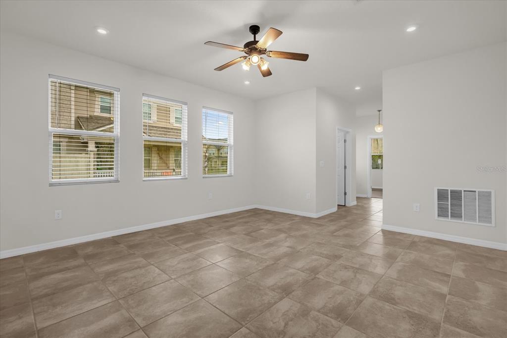 An empty room with light tile flooring, three windows, and a ceiling fan — 2444 VARENNA LOOP, KISSIMMEE, FL