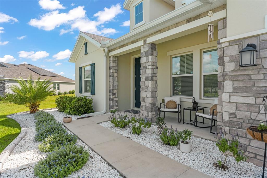 The exterior of a house features a stone-accented porch, a concrete walkway, and landscaped gravel — 6025 CLAYSTONE WAY, MOUNT DORA, FL