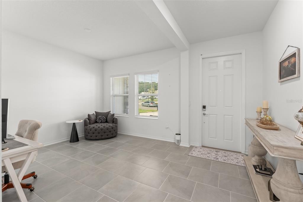A bright home office with tile flooring, a desk, a round armchair, and an entryway door — 6025 CLAYSTONE WAY, MOUNT DORA, FL