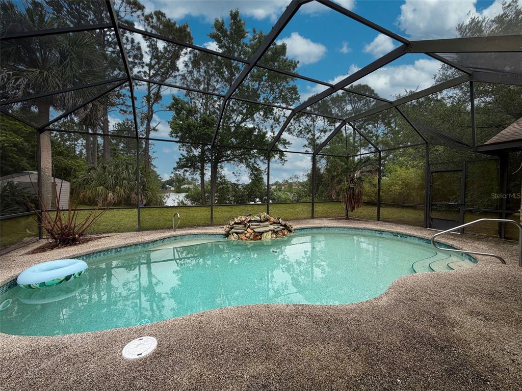 A screened-in swimming pool with a rock waterfall feature overlooks a grassy yard and trees — 51 FANSHAWE LANE, PALM COAST, FL