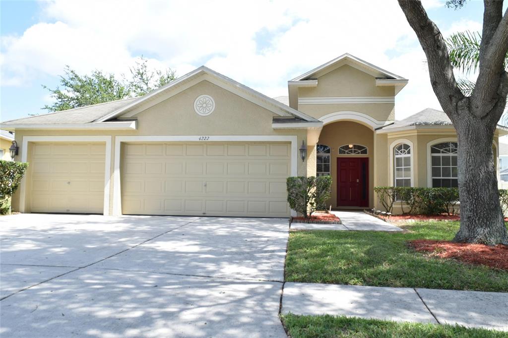A single-story tan house with a three-car garage and a red front door — 4222 BALINGTON DRIVE, VALRICO, FL