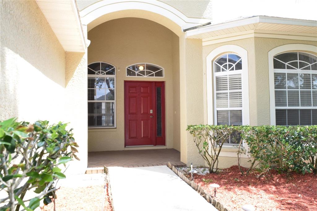 A red front door is centered under a covered entryway with arched windows and landscaping — 4222 BALINGTON DRIVE, VALRICO, FL