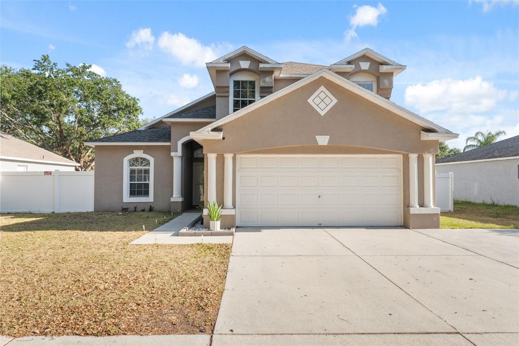 A two-story suburban house with a tan stucco exterior, a two-car garage, and columns — 3316 PINE TOP DRIVE, VALRICO, FL