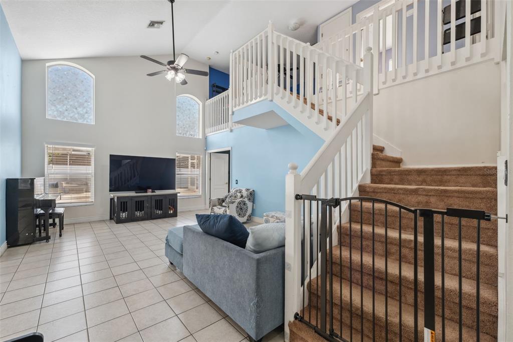 A living room with tile floors, a staircase with a baby gate, and high ceilings — 3316 PINE TOP DRIVE, VALRICO, FL
