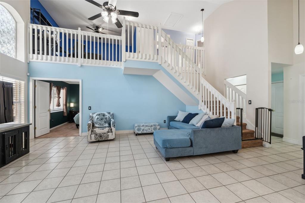 A living room with light blue walls, tile flooring, a staircase, and a loft balcony — 3316 PINE TOP DRIVE, VALRICO, FL