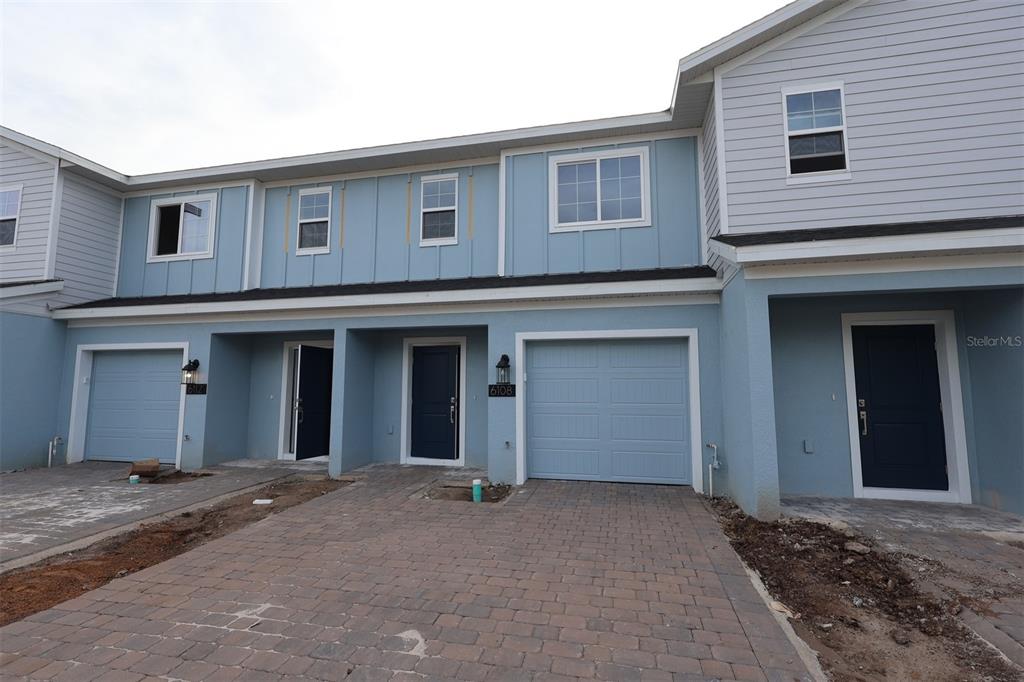 The exterior of a multi-unit townhouse complex features light blue siding, garages, and paved driveways — 6108 FELLOW WAGON WAY, ORLANDO, FL