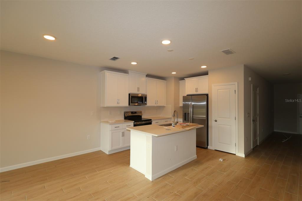 A kitchen with white cabinets, stainless steel appliances, a center island, and light wood flooring — 6108 FELLOW WAGON WAY, ORLANDO, FL