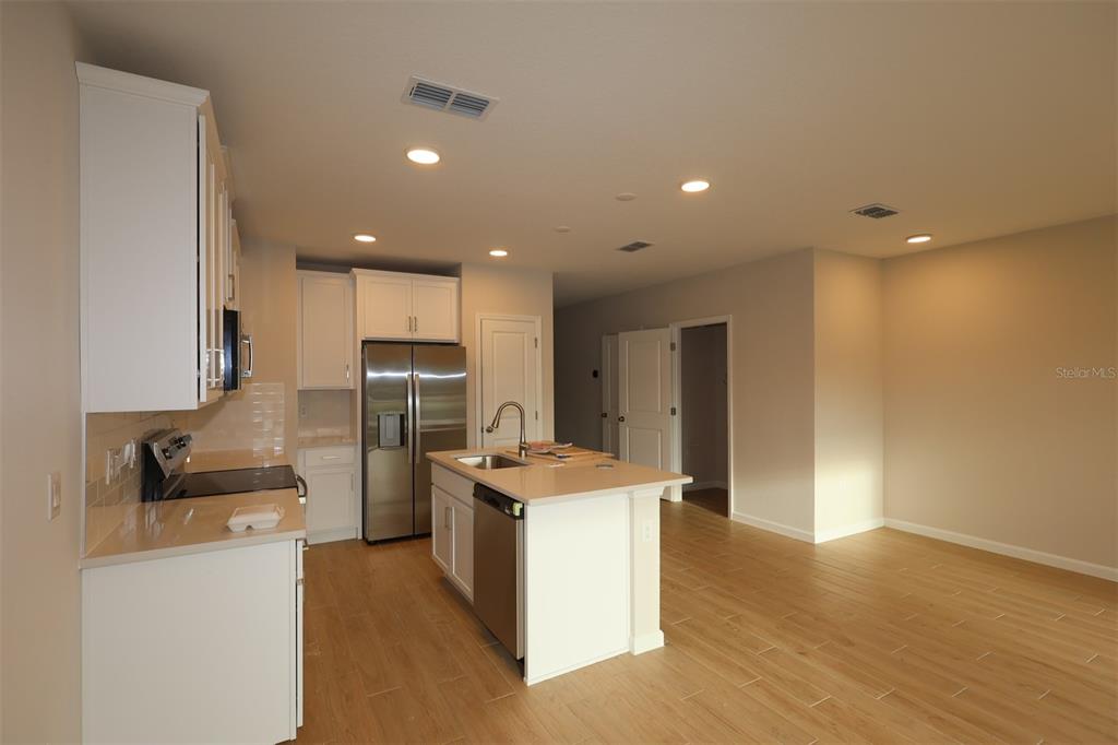A kitchen features white cabinets, stainless steel appliances, a center island, and light wood flooring — 6108 FELLOW WAGON WAY, ORLANDO, FL