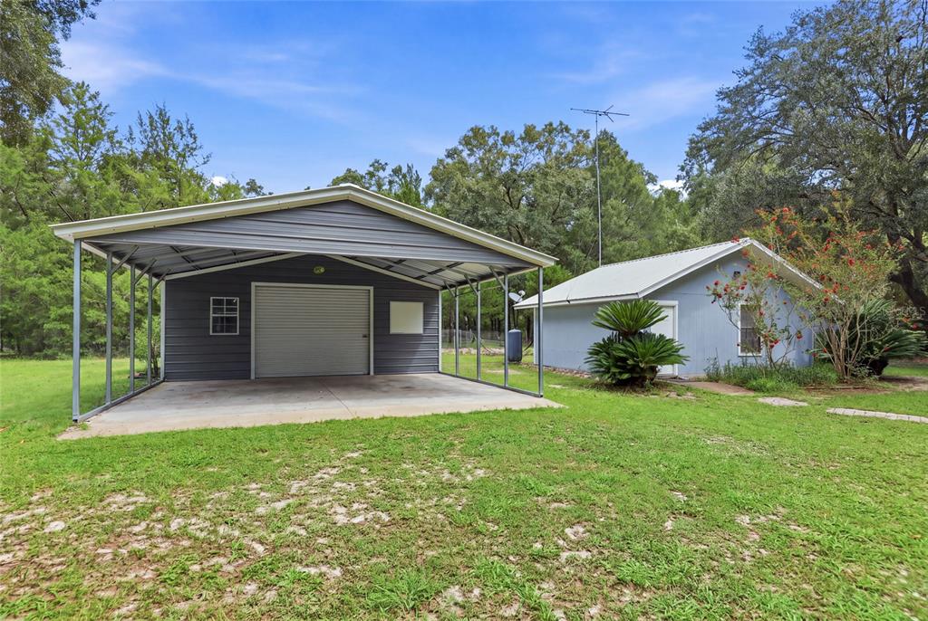 A metal carport stands next to a small light blue building on a grassy lot — 753 SW MAPLETON STREET, FORT WHITE, FL