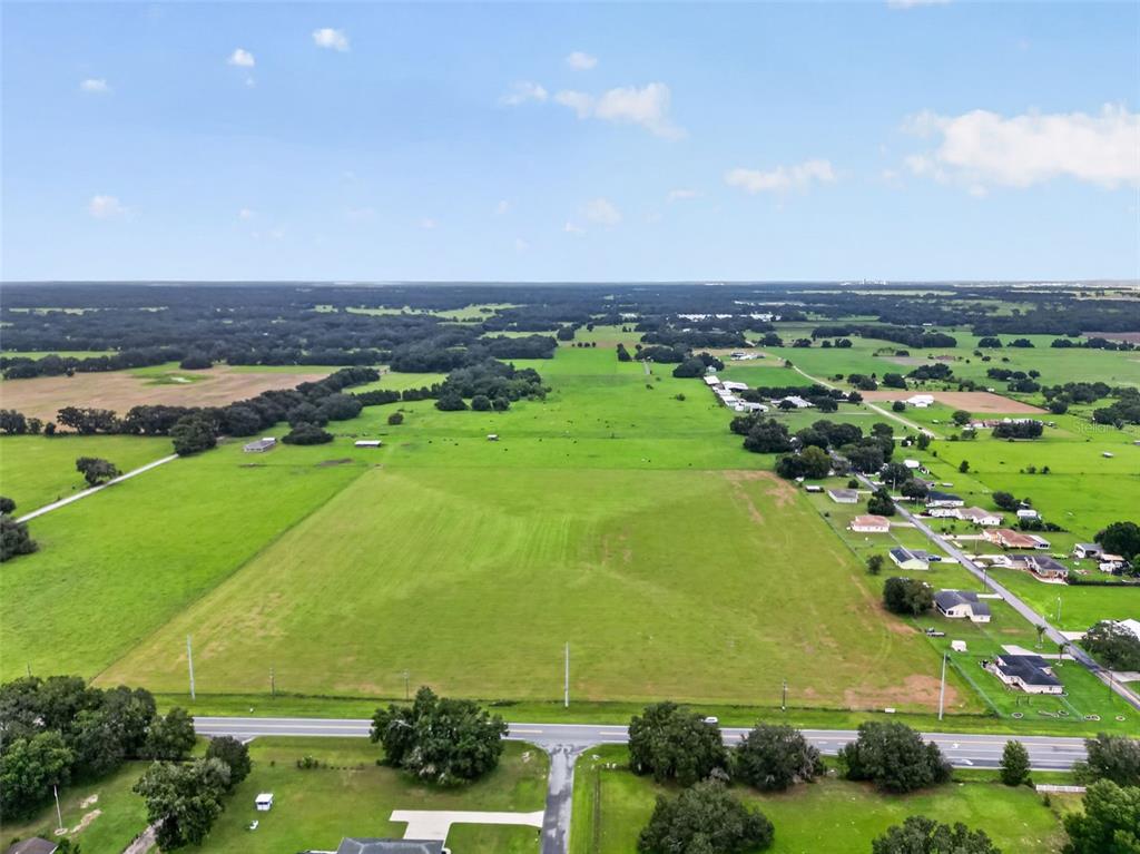 An aerial view shows a large, open green pasture bordered by a road and trees — TBD WC 48, BUSHNELL, FL