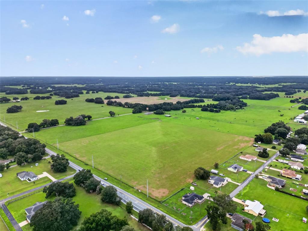 An aerial view shows a large, open green pasture bordered by a road and residential houses — TBD WC 48, BUSHNELL, FL